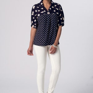 May include: A woman is wearing a black and white patterned blouse with a collar and white pants. She is wearing navy blue heels.