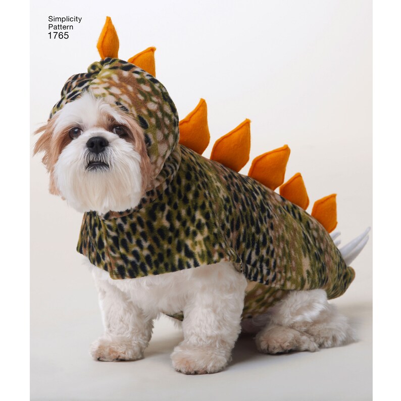 May include: A white dog wearing a green and brown dinosaur costume with orange spikes. The costume has a hood and a tail.