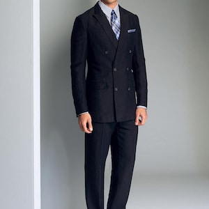 May include: A man wearing a black double-breasted suit with a white shirt and a patterned tie. He is standing in front of a white wall.