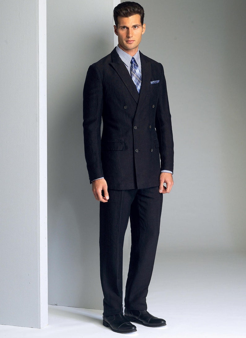 May include: A man wearing a black double-breasted suit with a white shirt and a patterned tie. He is standing in front of a white wall.