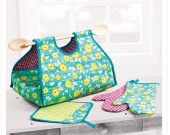 Op de afbeelding: Simplicity patroon S9528. Een gewatteerde draagtas met houten lepelhandvatten, bijpassende ovenwanten en een pannenlap. De tas en wanten hebben een blauwe achtergrond met gele bloempatronen. De pannenlap heeft een groen-wit geblokt patroon.