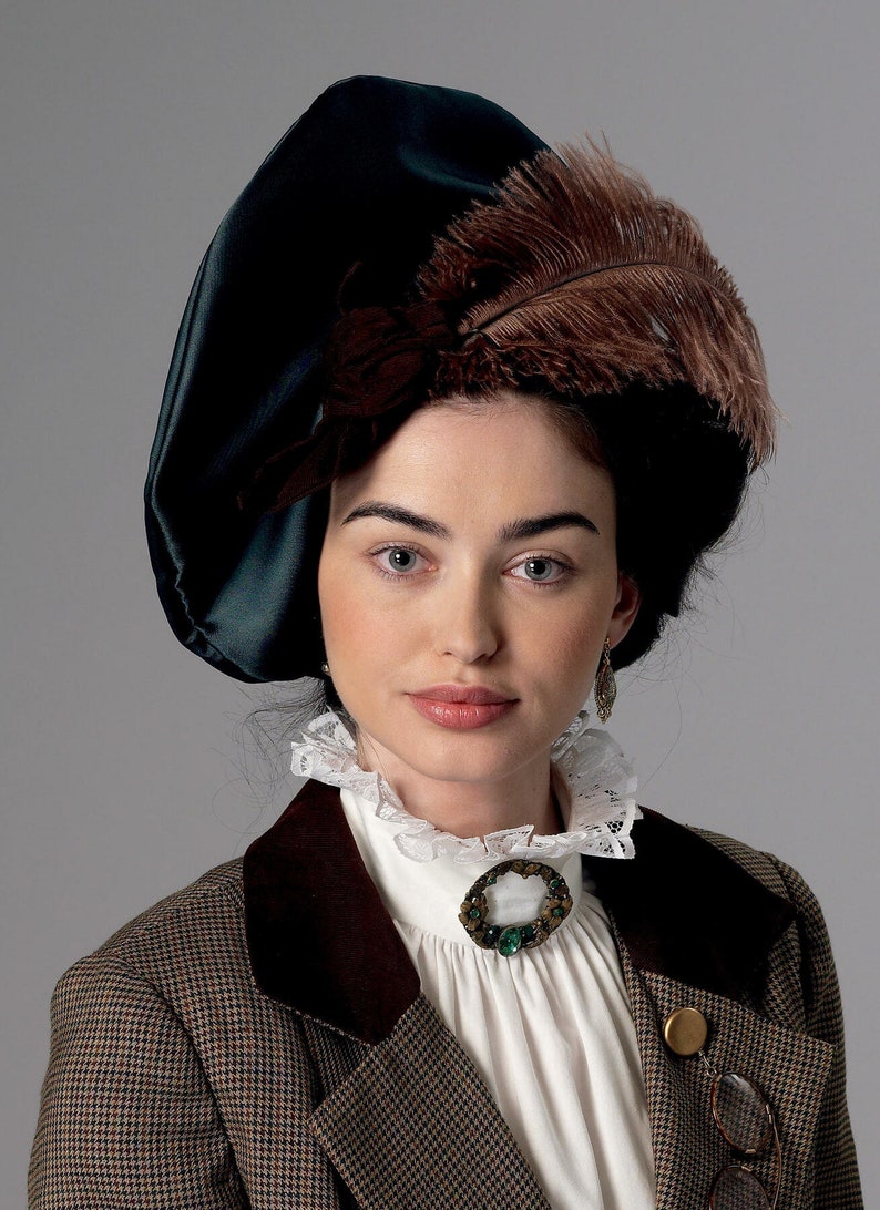 May include: A woman wearing a dark green hat with a large brown feather, a white ruffled collar, and a brown and tan tweed jacket. A decorative brooch with a green stone is pinned to the collar.