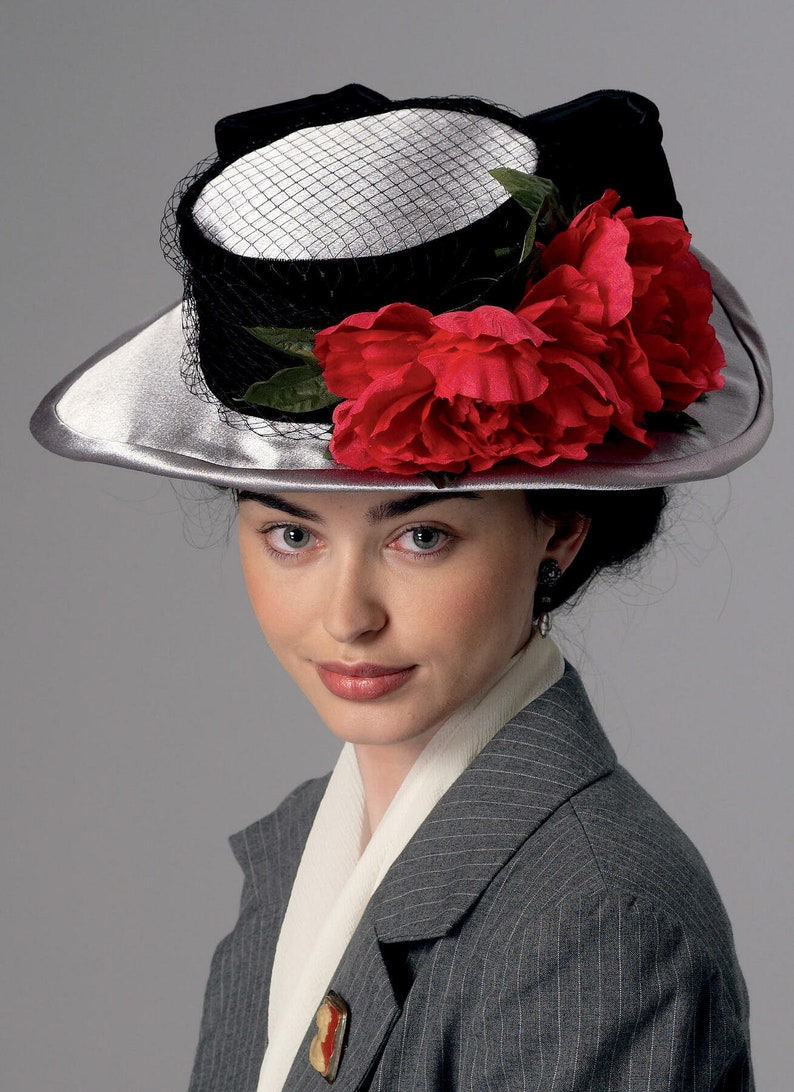 May include: A silver-brimmed hat with a black crown and a white top, adorned with a black veil and vibrant red fabric flowers. The hat is part of a vintage fashion ensemble, suitable for special occasions.