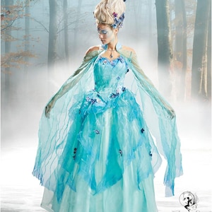 Puede incluir: Un patrón Simplicity para un disfraz de fantasía. La imagen presenta un vestido azul claro con capas de tela y detalles florales. La modelo lleva un tocado y una capa a juego. El logotipo de Simplicity y el número de patrón 8629 son visibles.