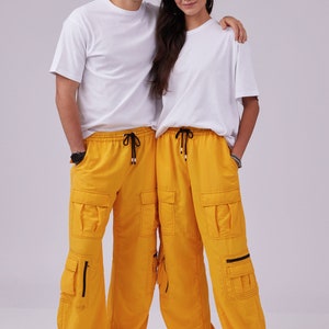 May include: Two people wearing white t-shirts and matching yellow cargo pants with black drawstrings. The pants have multiple pockets with zippers.
