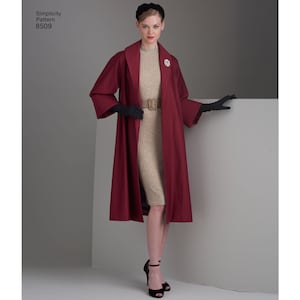 May include: A long, burgundy coat with a wide collar and long sleeves. The coat is belted at the waist and has a brooch on the left side. The model is wearing a beige dress and black heels.