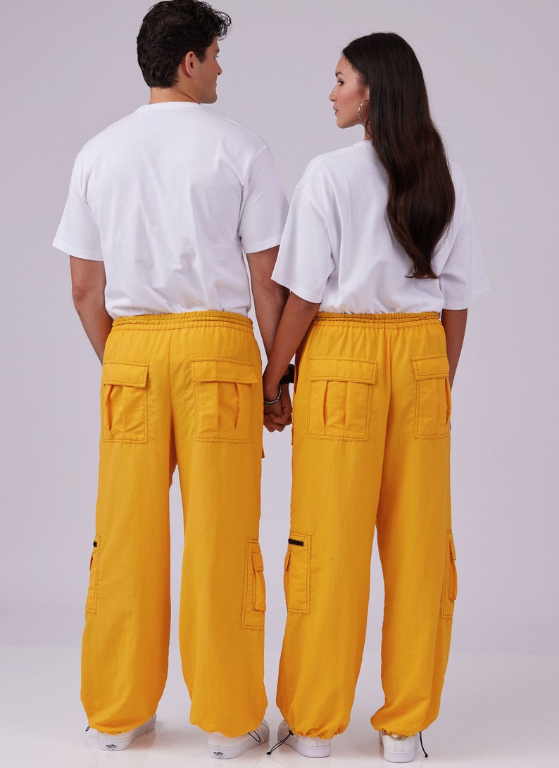 May include: Two people wearing white t-shirts and matching yellow cargo pants with black accents. They are standing back to back with their hands clasped together.