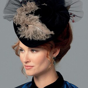 May include: A black velvet hat with a decorative arrangement of feathers and tulle. The hat features a wide brim and is adorned with a cluster of beige feathers and a delicate black tulle overlay. A vintage-inspired accessory.
