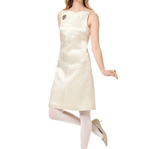 May include: A sleeveless white dress with a geometric pattern. The dress has a scoop neckline and a fitted silhouette. The model is wearing white tights and gold shoes.