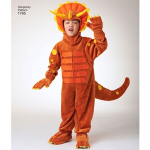 May include: A child wearing a brown and orange dinosaur costume with yellow accents. The costume includes a headpiece with horns and a tail. The costume is labeled "Simplicity Pattern 1765".