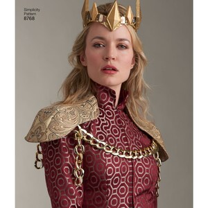 May include: A woman wearing a red and gold costume with a gold crown. The costume features a patterned fabric with a geometric design and a gold chain across the chest. The crown has a pointed design with gold accents.