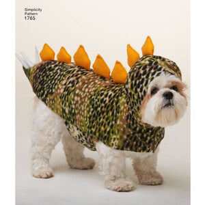 May include: A white dog wearing a green and brown camouflage dinosaur costume with orange spikes on the back.