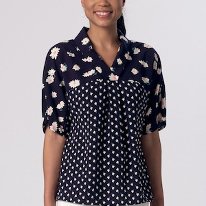 May include: A navy blue and white patterned blouse with a v-neck and short sleeves. The blouse has a floral pattern on the top half and a smaller white dot pattern on the bottom half.