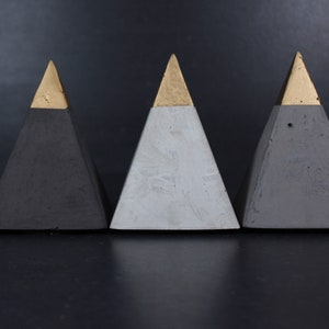 Może przedstawiać: Trzy betonowe piramidy ze złotymi wierzchołkami. Piramidy są czarne, szare i białe.