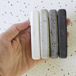 Four concrete samples in different shades of gray, from white to charcoal, held in a hand.