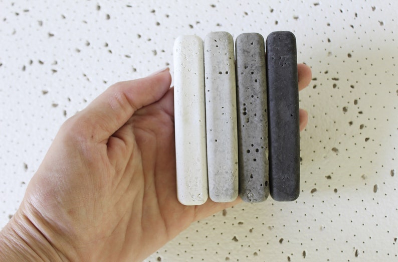 Four concrete samples in different shades of gray, from white to charcoal, held in a hand.