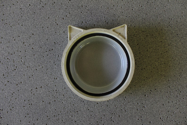 K&ouml;nnte beinhalten: Wei&szlig;e Keramik Sch&uuml;ssel in Katzenform mit schwarzem Rand. Die Sch&uuml;ssel ist leer und hat eine glatte, gl&auml;nzende Oberfl&auml;che.