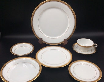 May include: Set of six white porcelain dinnerware pieces with gold trim. The set includes a large dinner plate, a salad plate, a soup bowl, a bread and butter plate, a teacup, and a saucer.