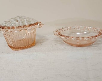 May include: Two vintage pink glass bowls with scalloped edges. The larger bowl has a raised center for holding flowers.