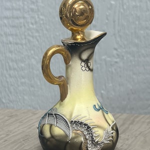 May include: A small, yellow ceramic bottle with a gold lid and a dragon design. The bottle has a gold handle and a floral design on the neck.