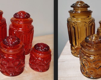 May include: Set of four glass canisters with a moon and star pattern. The canisters are in two colors: red and amber.