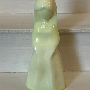 May include: A pale yellow ceramic figurine of a woman with long hair and a flowing dress.