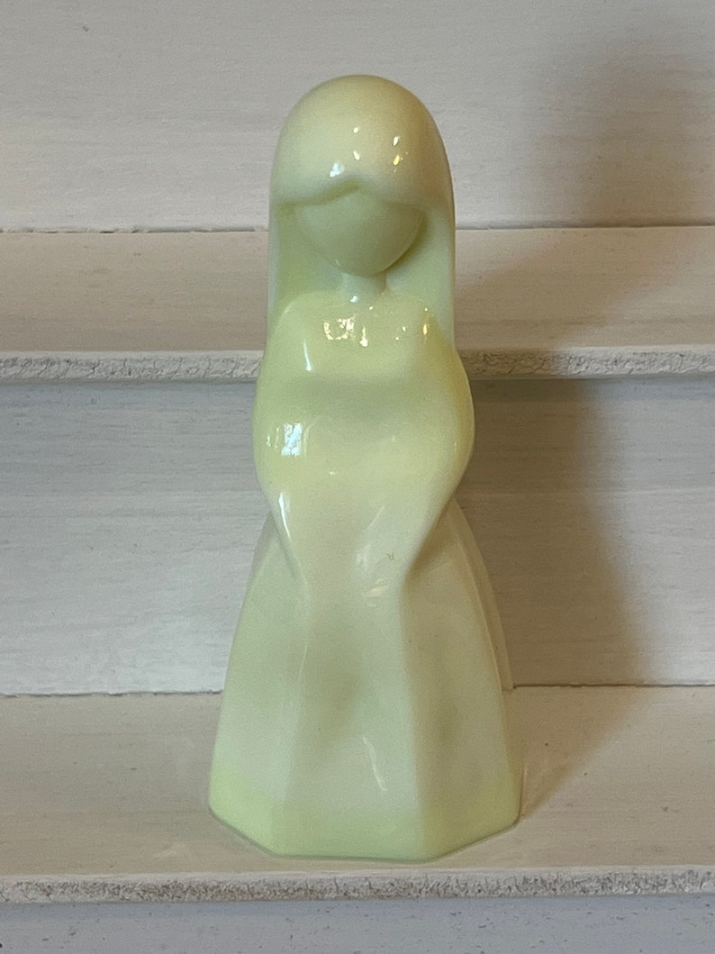 May include: A pale yellow ceramic figurine of a woman with long hair and a flowing dress.
