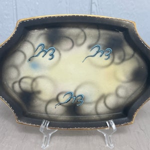May include: A black and white oval serving tray with a gold rim and a swirl design. The tray has three blue and white stylized swirls on the surface.