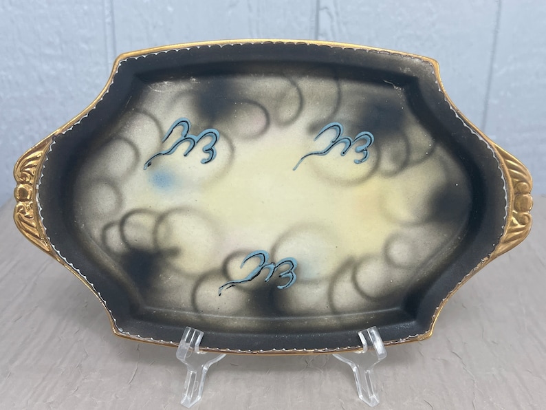 May include: A black and white oval serving tray with a gold rim and a swirl design. The tray has three blue and white stylized swirls on the surface.