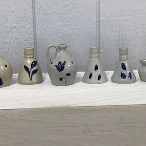 May include: Set of seven small, hand-painted ceramic pottery pieces in shades of gray and blue with floral designs. The pieces include a pitcher, a vase, and five small jars.