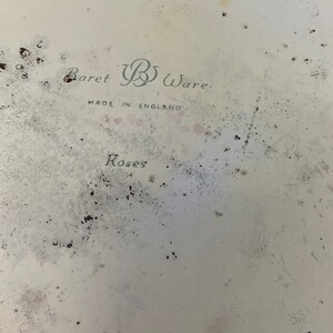 May include: A white ceramic plate with a faded green and black design. The plate has the text "Baret B Ware. Made in England. Roses" printed on it.