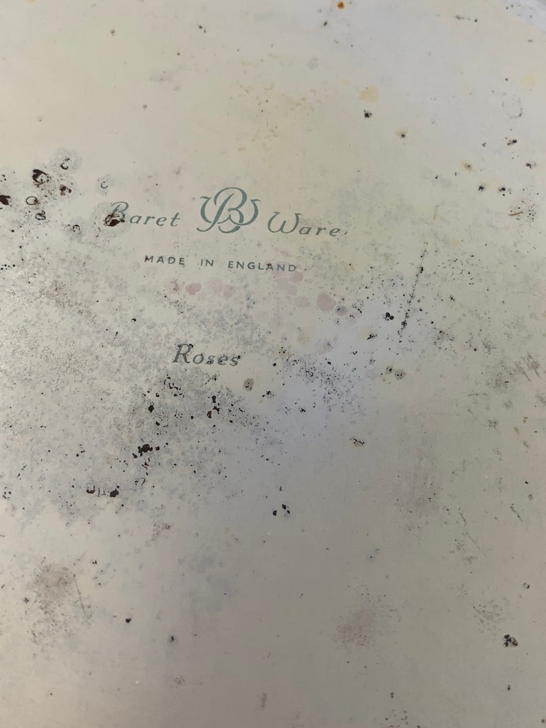 May include: A white ceramic plate with a faded green and black design. The plate has the text "Baret B Ware. Made in England. Roses" printed on it.