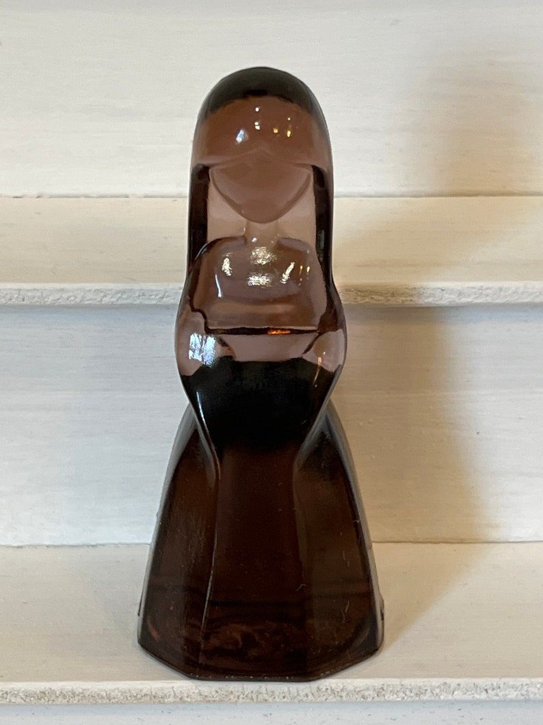 Pu&ograve; includere: Una bottiglia vintage in vetro marrone a forma di figura stilizzata. La bottiglia ha una testa arrotondata, una vita stretta e una gonna svasata. Il vetro &egrave; di colore marrone traslucido.