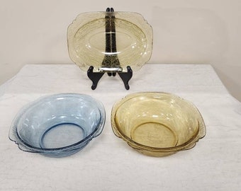 May include: Three glass bowls, one blue, one yellow, and one clear, with a textured pattern. The bowls are on a white surface.