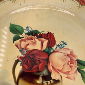 May include: A vintage tin tray with a red and gold border. The tray features a painted image of a bouquet of pink and red roses in a gold vase.