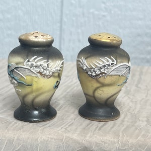 May include: A pair of ceramic salt and pepper shakers with a dragon design. The shakers are black, white, and yellow with gold accents.