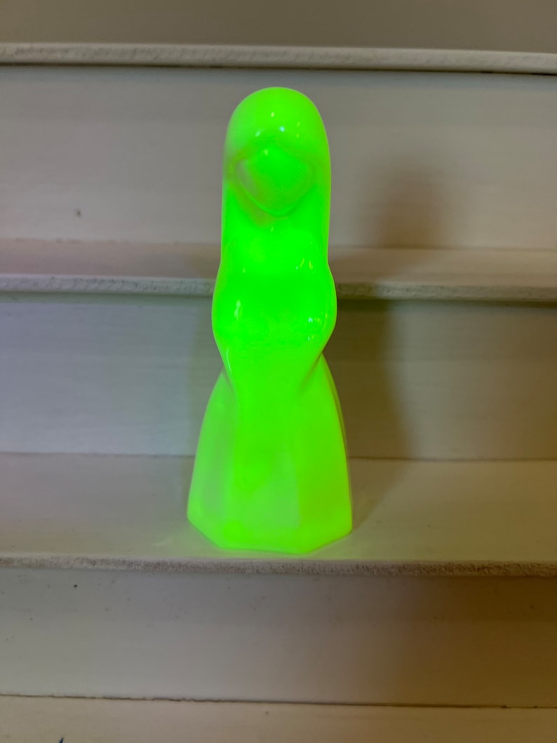 May include: A glowing green ceramic figurine of a woman with long hair and a flowing dress.