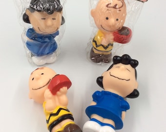May include: Four Peanuts character figurines, including Lucy, Linus, and two versions of Sally. The figurines are made of plastic and are in their original packaging. The figurines are all wearing their signature clothing.