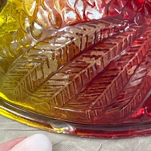 K&ouml;nnte beinhalten: Nahaufnahme einer dekorativen Glasschale mit Federdesign. Die Schale wechselt von Gelb &uuml;ber Orange zu Rot. Das Glas hat eine strukturierte Oberfl&auml;che mit detaillierten Federmustern.