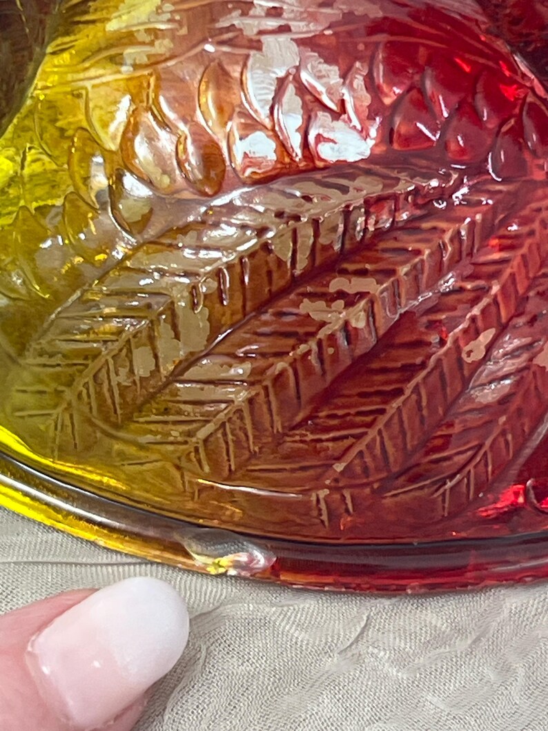 K&ouml;nnte beinhalten: Nahaufnahme einer dekorativen Glasschale mit Federdesign. Die Schale wechselt von Gelb &uuml;ber Orange zu Rot. Das Glas hat eine strukturierte Oberfl&auml;che mit detaillierten Federmustern.