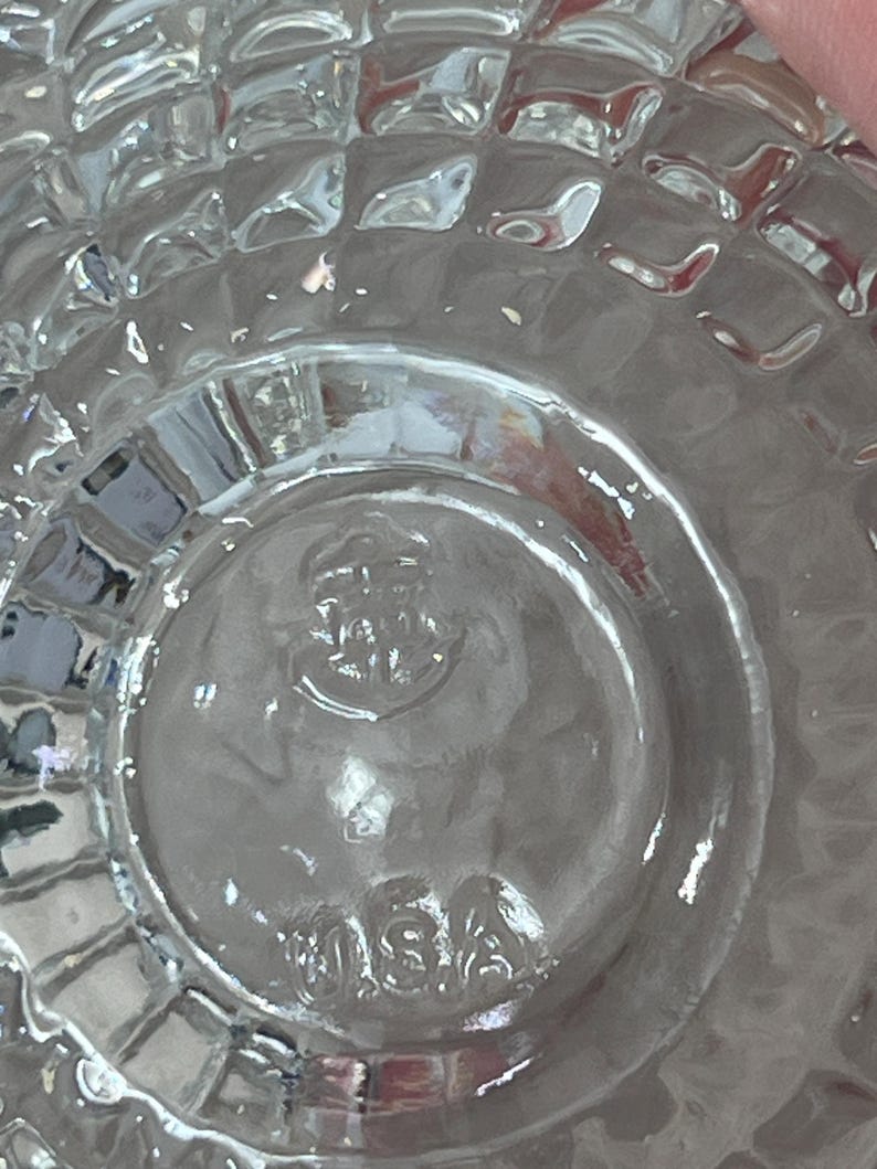 K&ouml;nnte beinhalten: Klares Glasobjekt mit einem strukturierten, gitterartigen Muster. Der Boden hat ein kreisf&ouml;rmiges Design mit dem gepr&auml;gten Text "USA". Das transparente Objekt l&auml;sst Licht durch und scheint ein Glaswarenst&uuml;ck zu sein.
