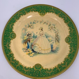 May include: A vintage metal serving tray with a green and gold border. The center of the tray features a painted image of a woman in a white dress standing in a garden.