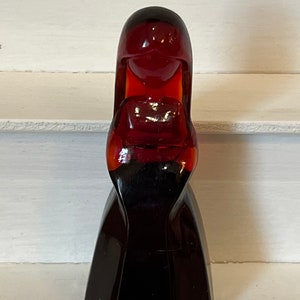 May include: A dark red glass figurine of a woman with long hair and a dress. The figurine is made of a dark red glass and has a glossy finish.