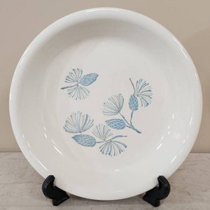 May include: A white ceramic serving dish with a blue and white pine cone design. The dish is on a black stand.