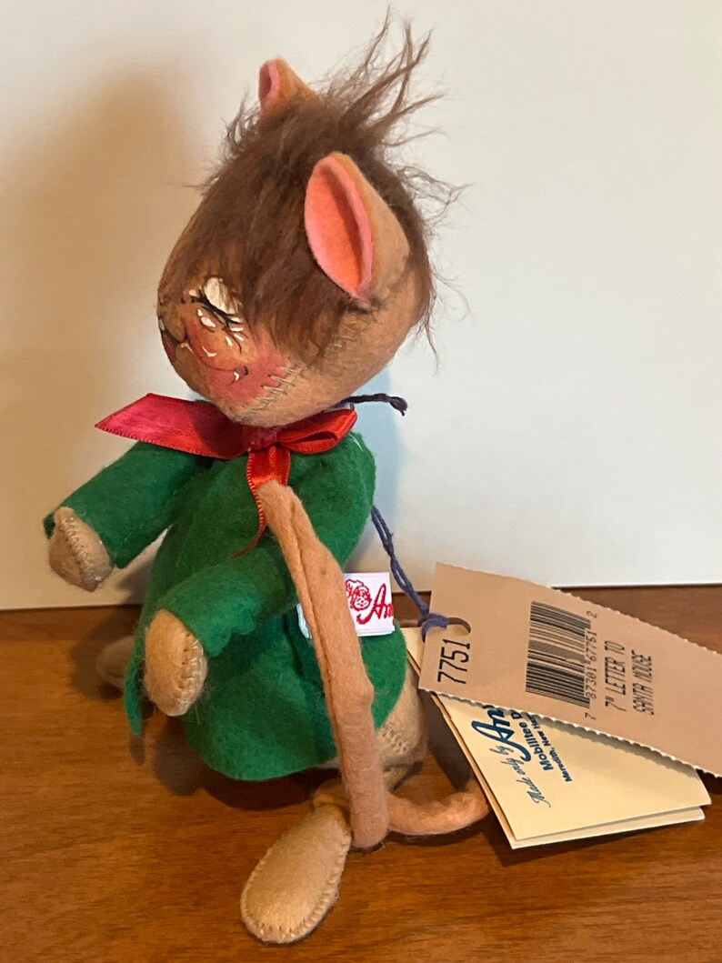K&ouml;nnte beinhalten: Eine braune und beige Filzmaus, die ein gr&uuml;nes Kleid mit einer roten Schleife tr&auml;gt. Die Maus hat einen langen Schwanz und h&auml;lt ein Schild mit der Aufschrift "7" Brief an den Weihnachtsmann Maus".