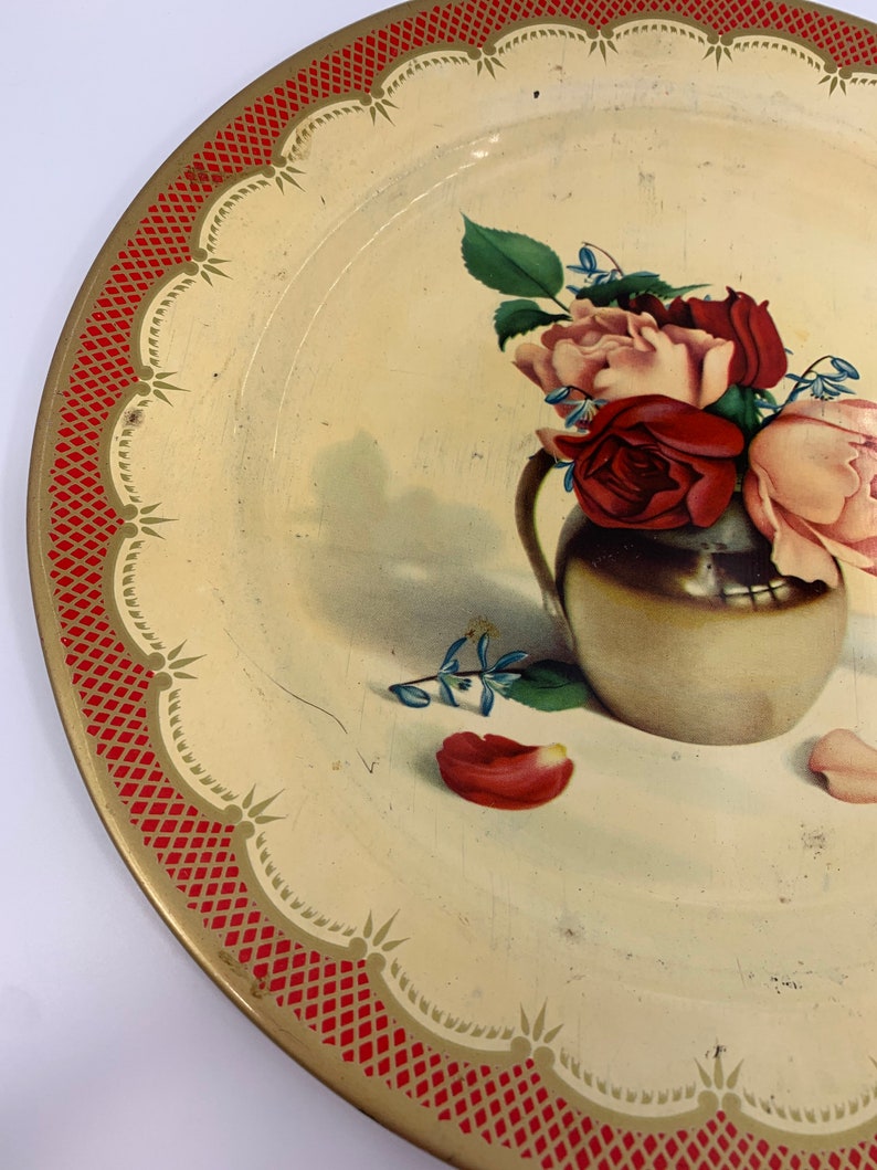 May include: A vintage metal serving tray with a red and gold border. The tray features a painted image of a bouquet of pink and red roses in a gold vase.
