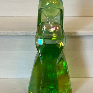 Pu&ograve; includere: Una statuetta in vetro verde iridescente raffigurante una donna in un lungo abito. La statuetta ha una lunga acconciatura e un'espressione serena. Il vetro ha un effetto cangiante multicolore, con sfumature di blu, viola e oro. La statuetta &egrave; alta circa 15 cm.