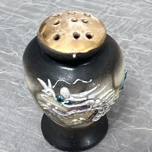 May include: A black ceramic salt shaker with a gold lid and a white dragon design. The lid has holes for dispensing salt.