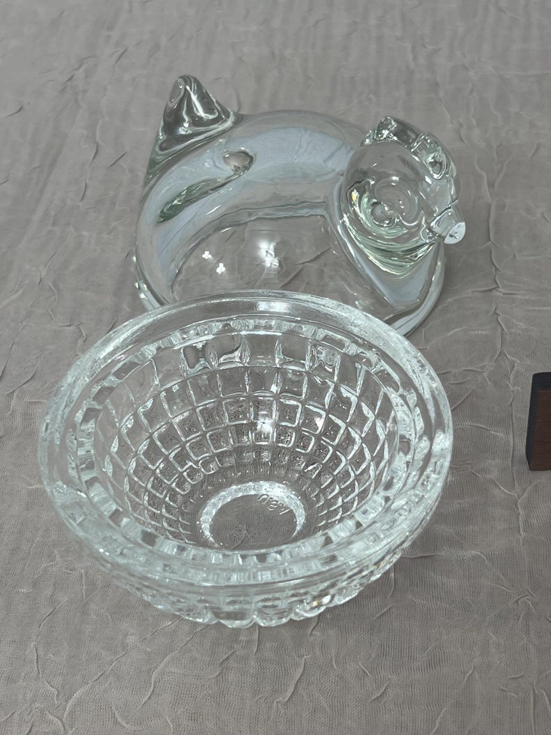 K&ouml;nnte beinhalten: Klarer Glasbeh&auml;lter in Schweineform mit Deckel und eine kleine, klare Glasschale mit einem strukturierten, gitterartigen Muster. Der Schweinebeh&auml;lter hat eine detaillierte Schnauze und Ohren. Die Sch&uuml;ssel ist rund und hat einen dekorativen Rand.