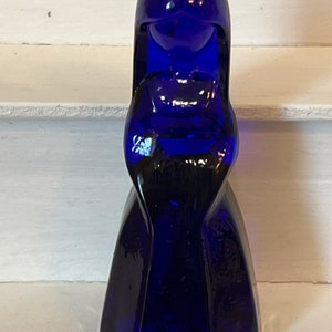 May include: A cobalt blue glass figurine of a woman with a long dress and a simple face.